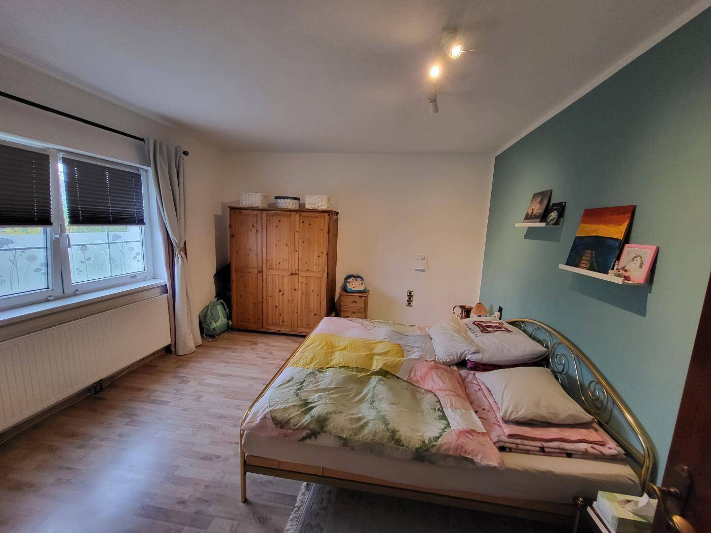 Schlafzimmer mit Holzboden, Kleiderschrank und einer farbigen Akzentwand.