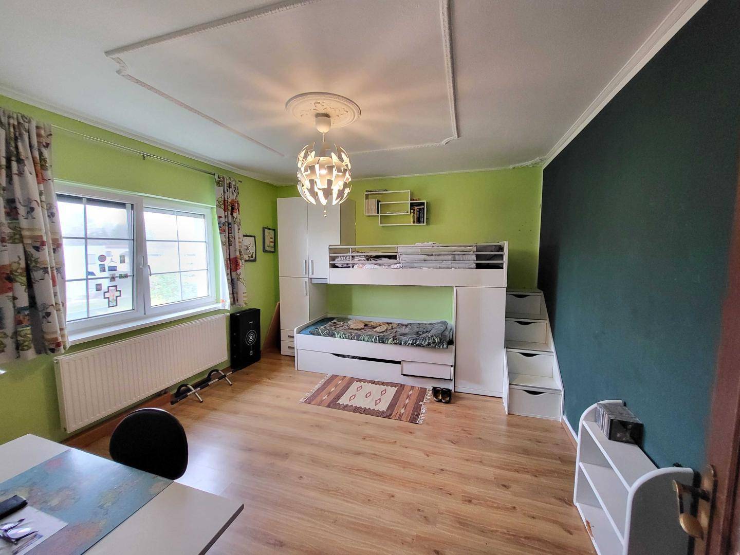 Kinderzimmer mit Etagenbett, Holzboden und farbigen Wänden in Grün und Dunkelgrün.