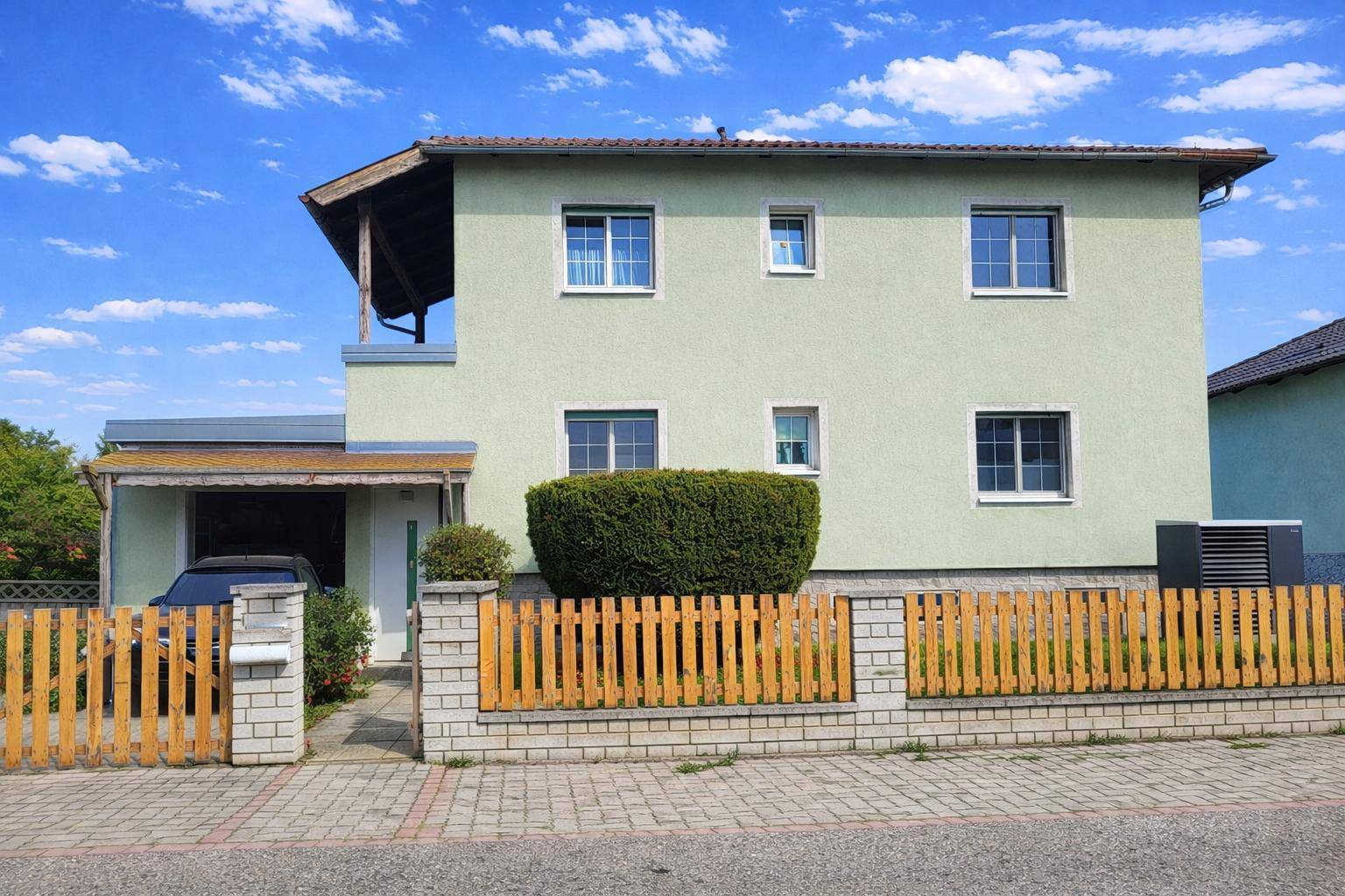 Vorderansicht des Hauses mit Zaun, Carport und gepflegter Hecke.