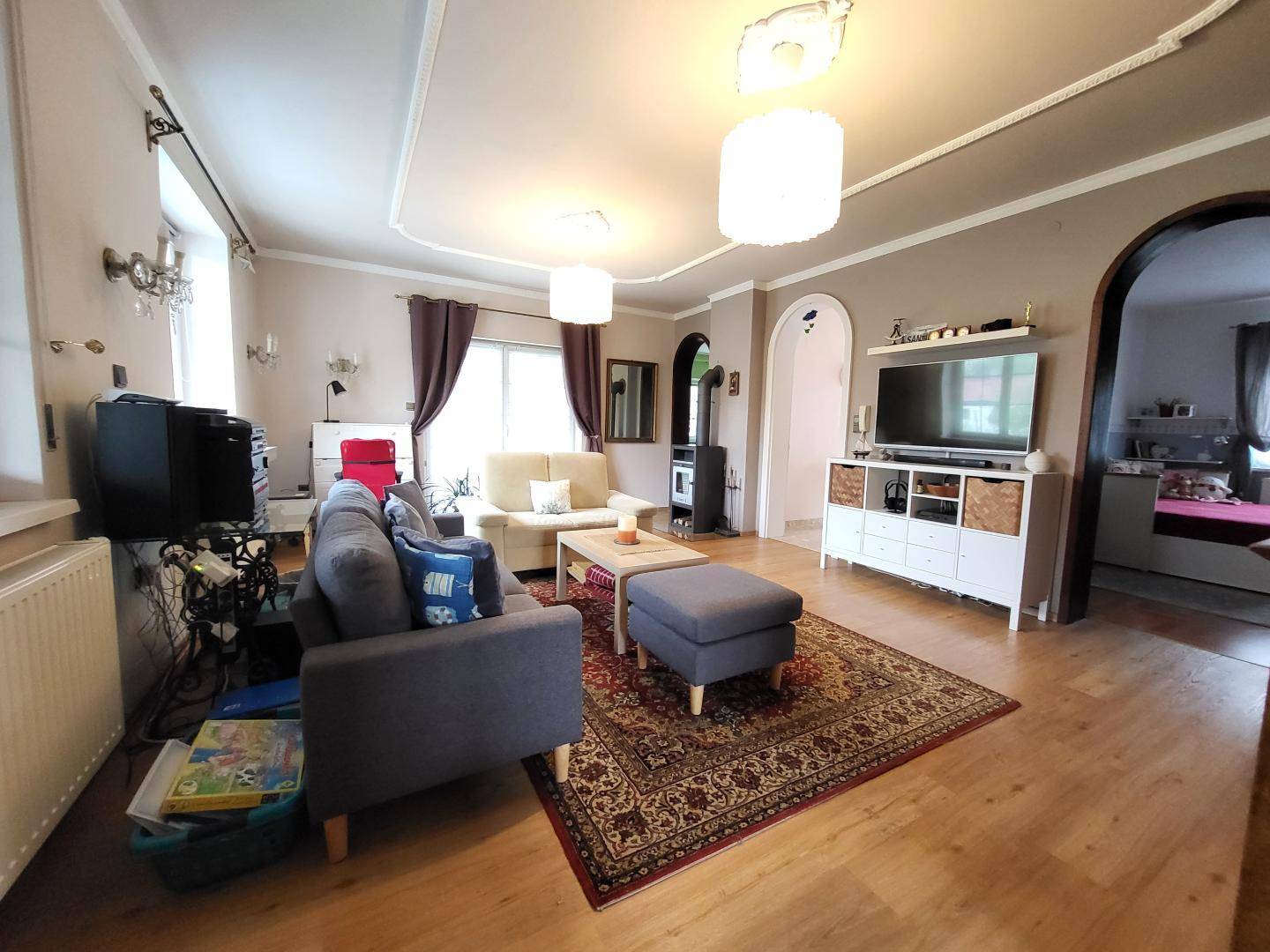 Gemütliches Wohnzimmer mit Sofa, Teppich und Holzboden, durch einen Bogen verbunden.