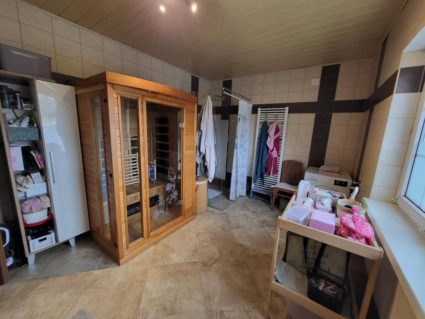 Badezimmer mit integrierter Sauna, Fliesenboden und Fenster für Tageslicht.