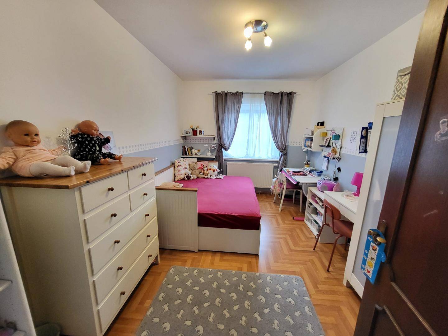 Kinderzimmer mit Holzboden, Schreibtisch und Spielzeug, hell und freundlich gestaltet.