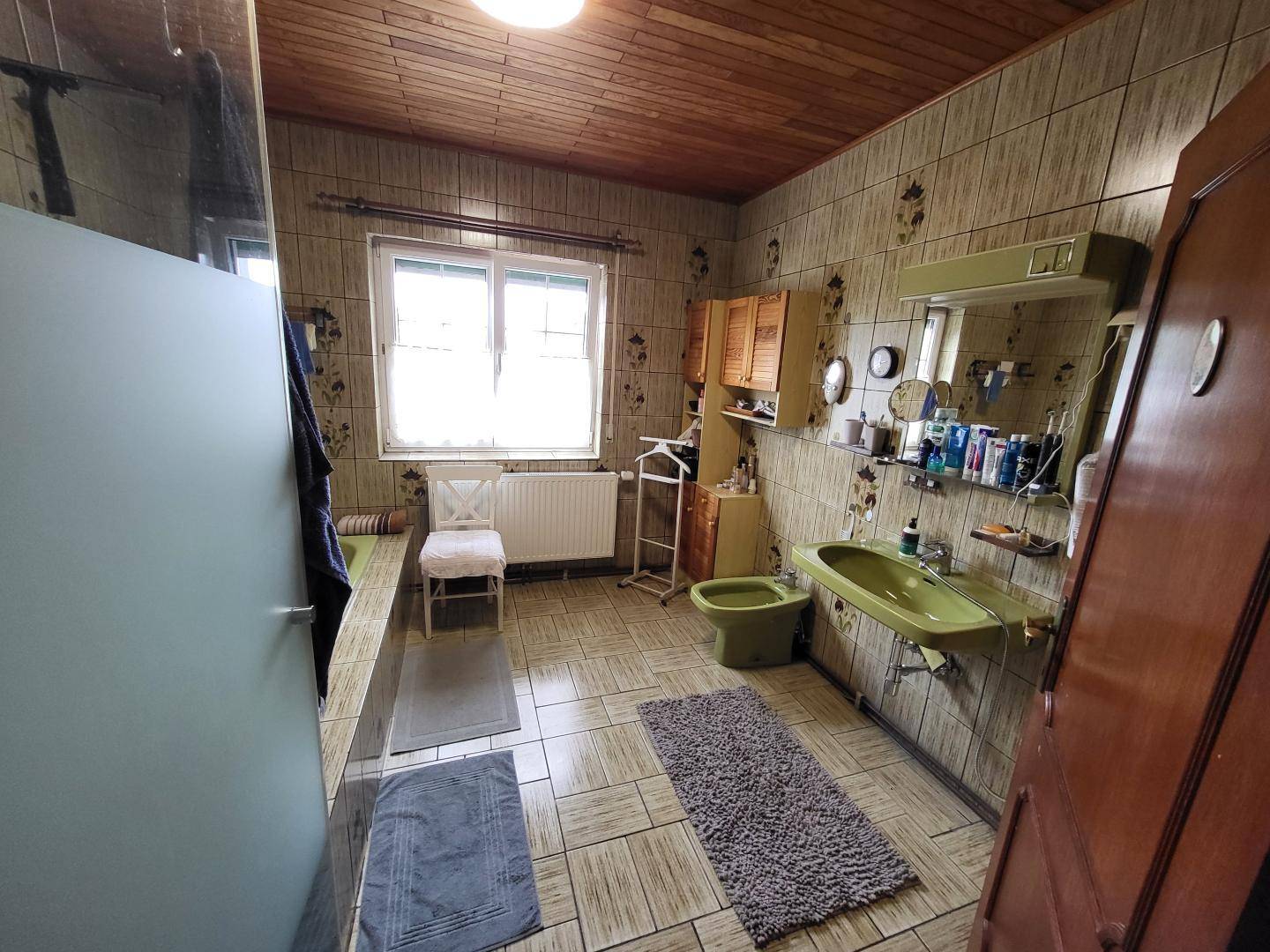 Badezimmer im 80er-Jahre-Stil mit grünen Sanitärobjekten, Fliesen und Holzdecke.