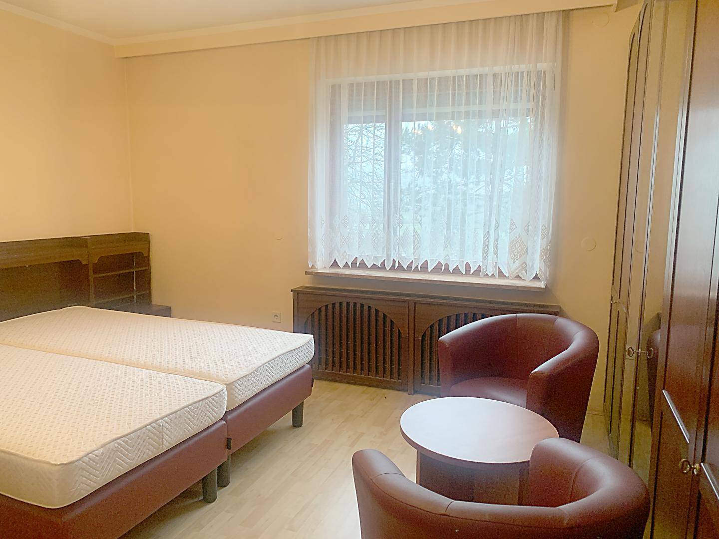 Schlafzimmer mit zwei Einzelbetten, Holzmöbeln und einem Fenster mit Vorhängen.