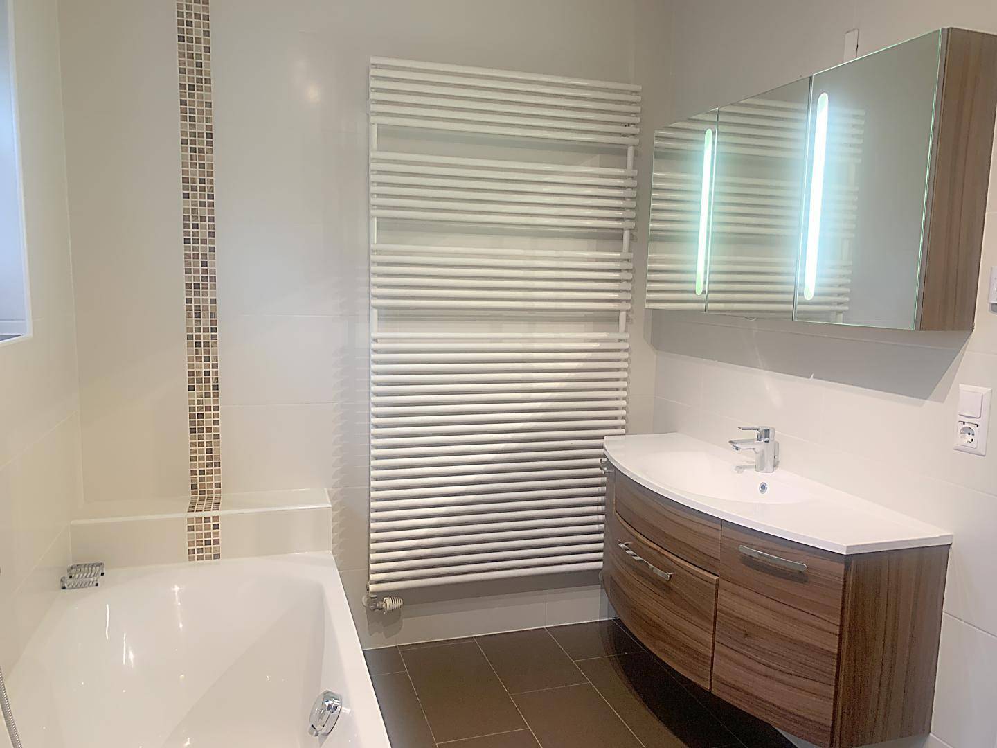 Modernes Badezimmer mit Badewanne, Waschtischunterschrank und beheiztem Handtuchhalter.
