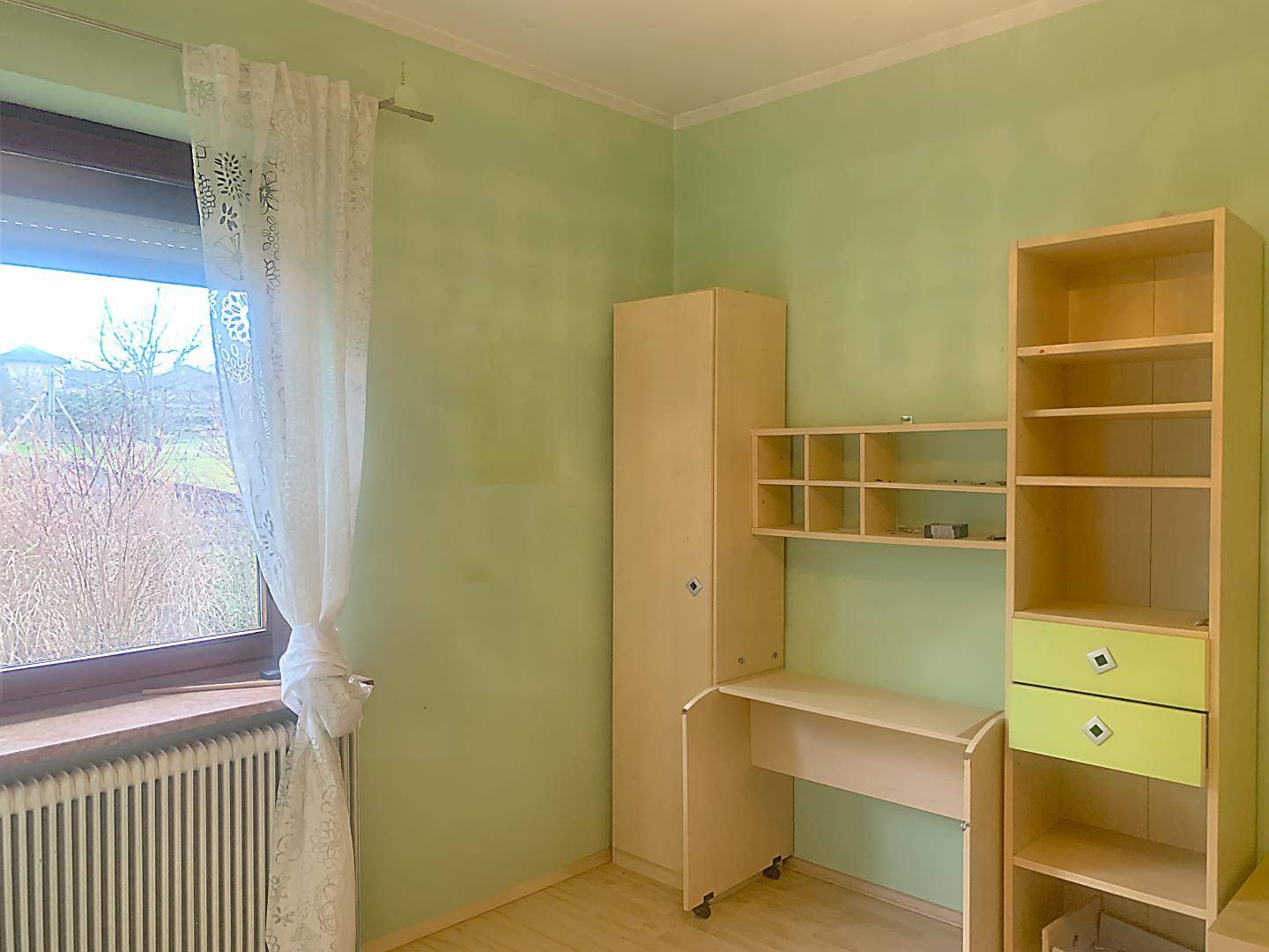 Kinderzimmer mit hellem Holzmobiliar, Schreibtisch und grünen Wänden.