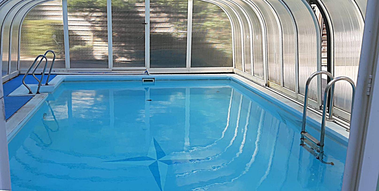Überdachtes Schwimmbad mit klarem Wasser und Sternenmuster auf dem Boden.