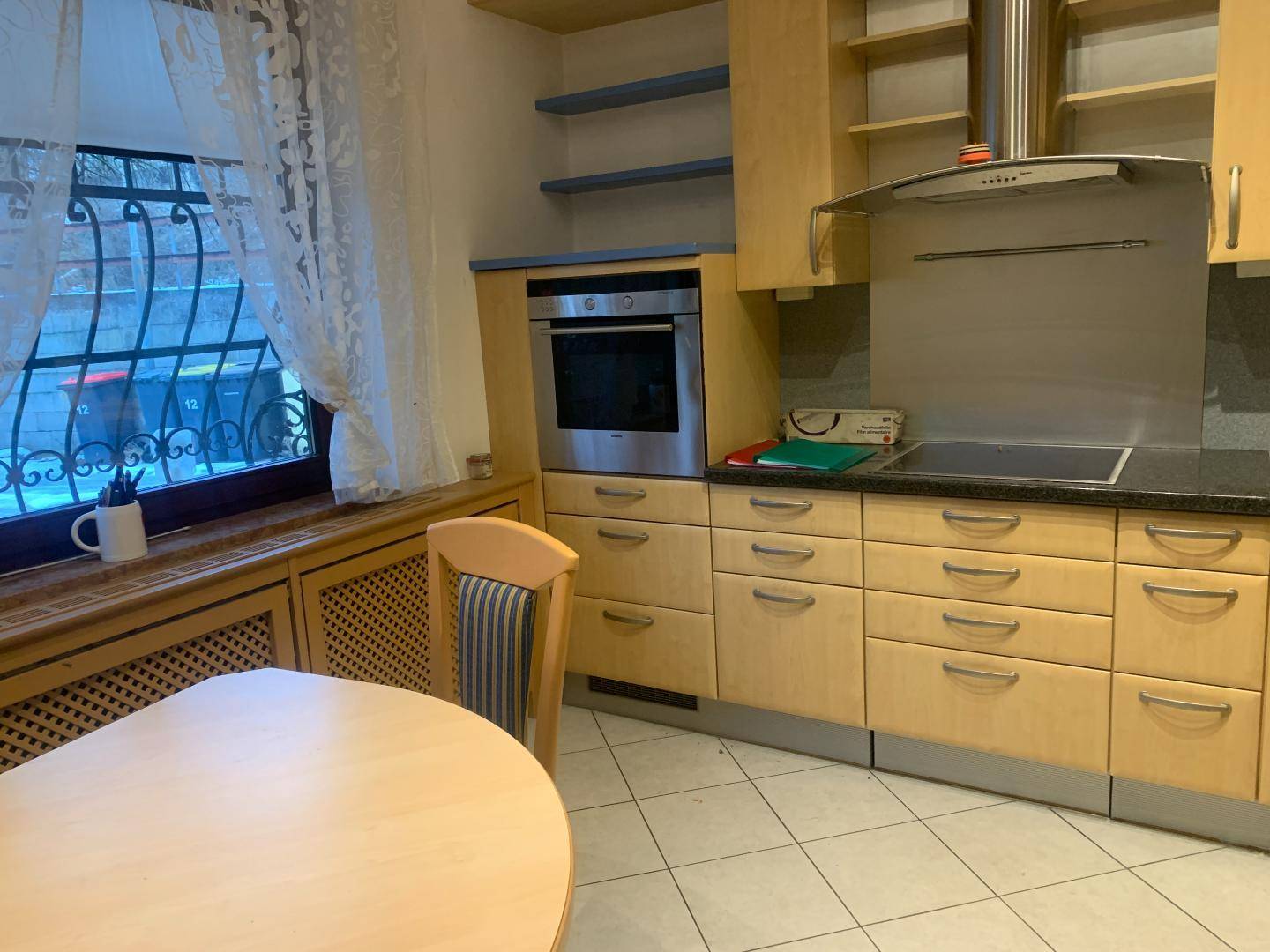 Gemütliche Wohnküche mit Esstisch, Holzschränken und Blick durch das Fenster ins Freie.