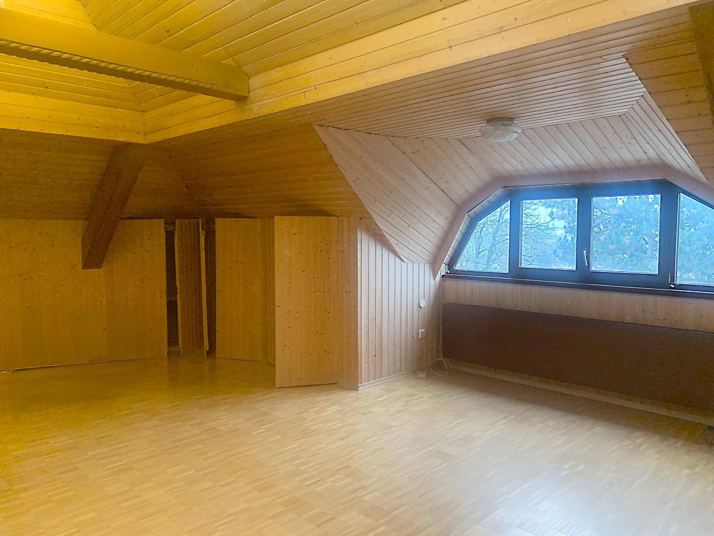 Geräumiger Dachbodenraum mit Holzvertäfelung, schrägen Decken und großen Fenstern.
