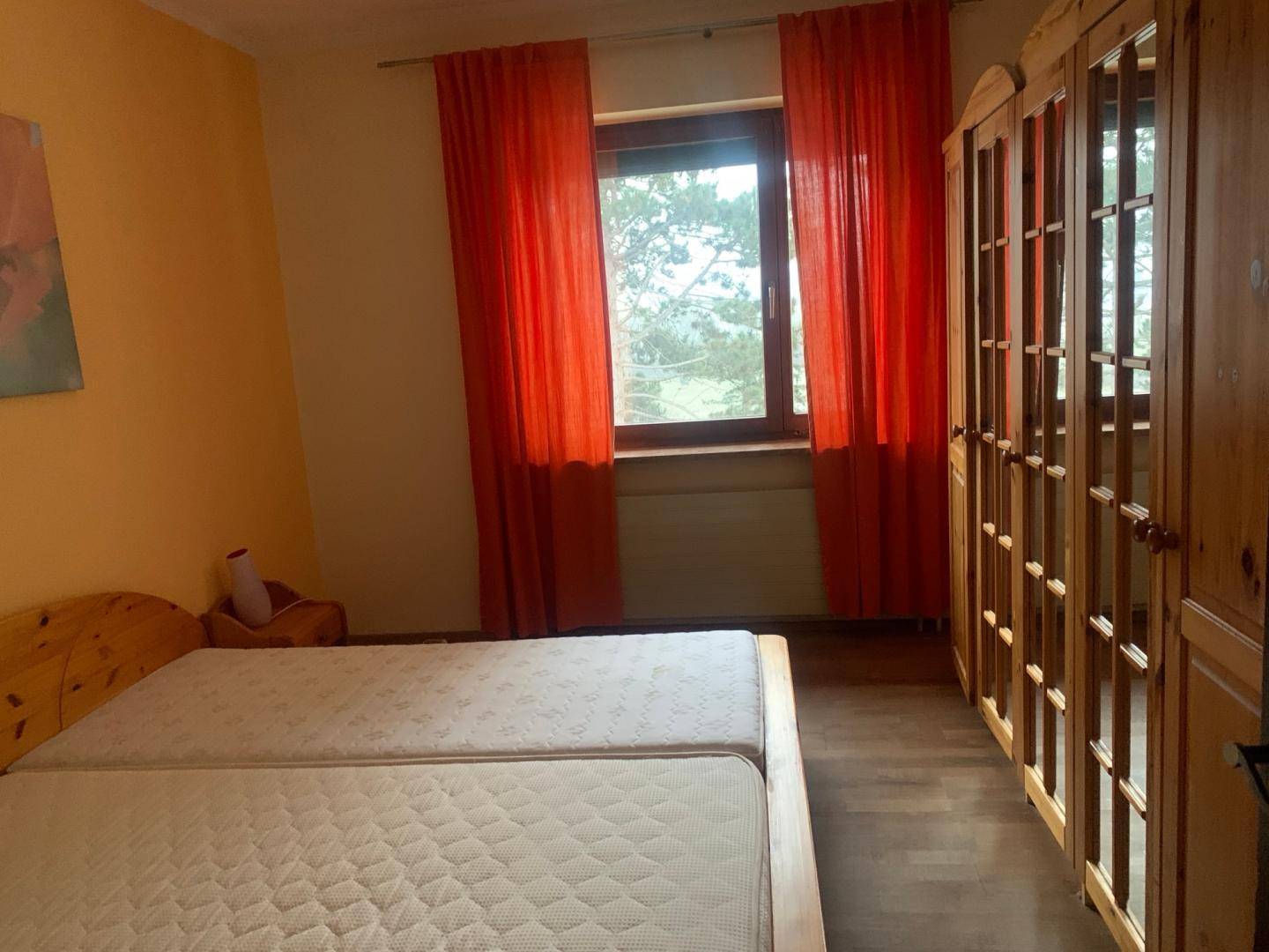 Schlafzimmer mit zwei Einzelbetten, Holzschrank und farbenfrohen Vorhängen am Fenster.