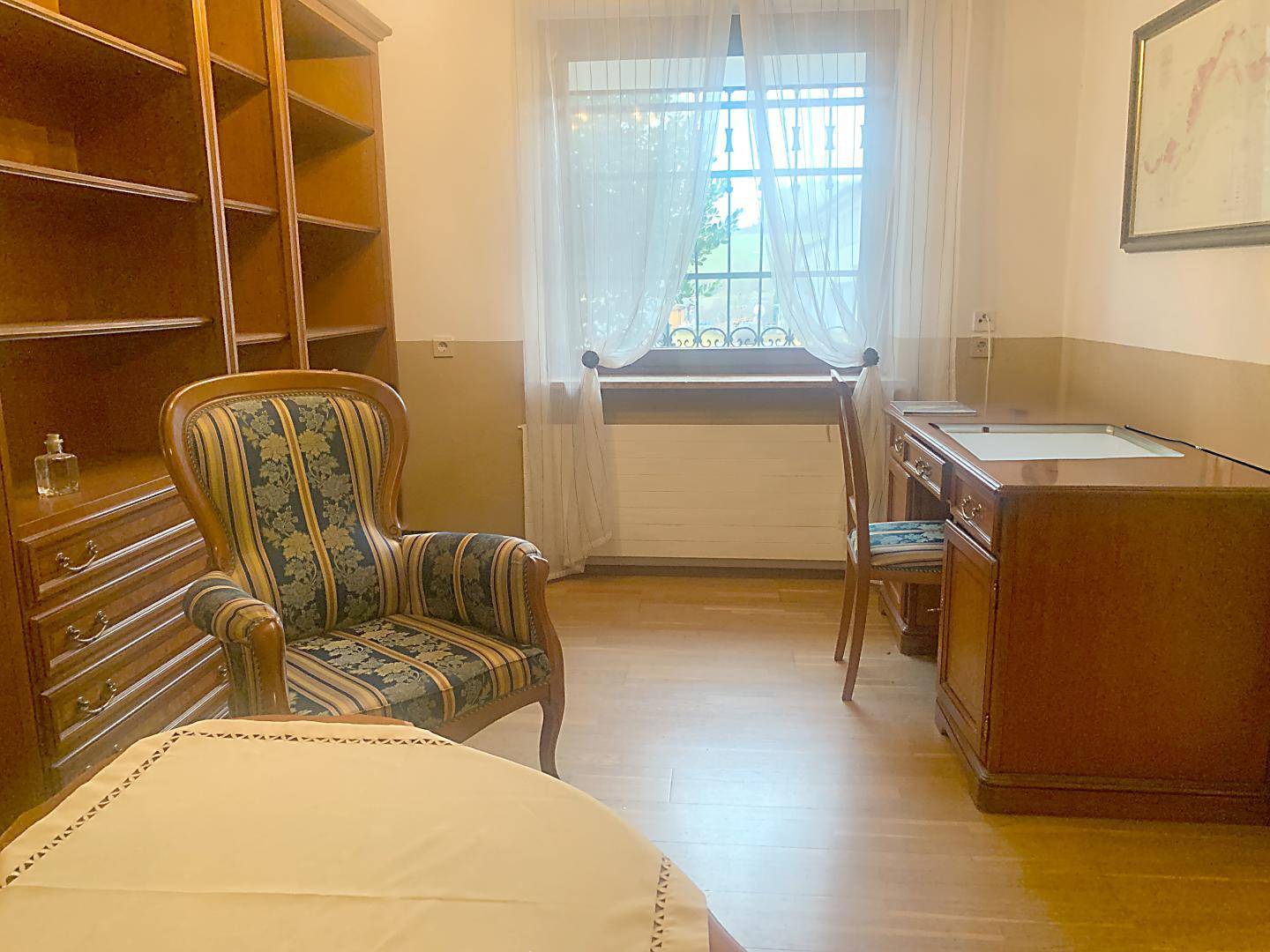 Helles Arbeitszimmer mit Holzmöbeln, Bücherregal und Blick ins Grüne durch das Fenster.