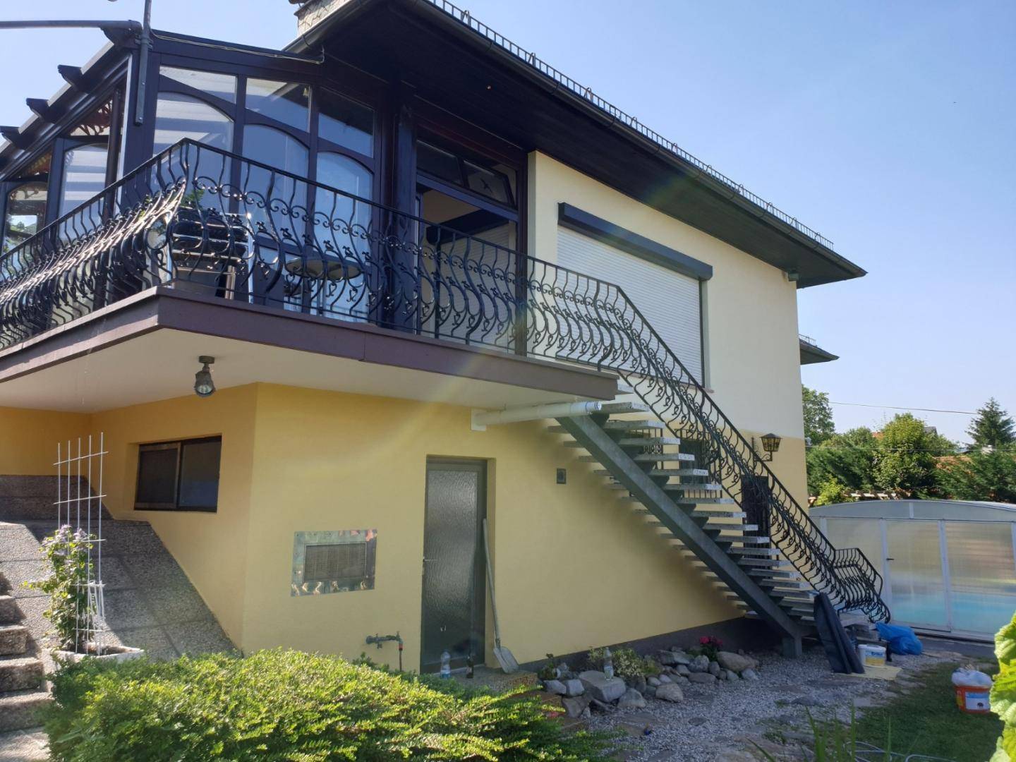 Seitenansicht des Hauses mit Außentreppe, verglastem Anbau und schmiedeeisernem Geländer.