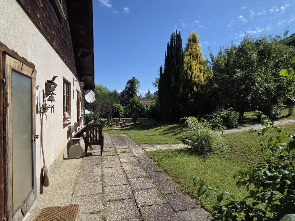 Sonniger Terrassenbereich mit Steinplatten und einer Holzbank, umgeben von üppigem Grün.