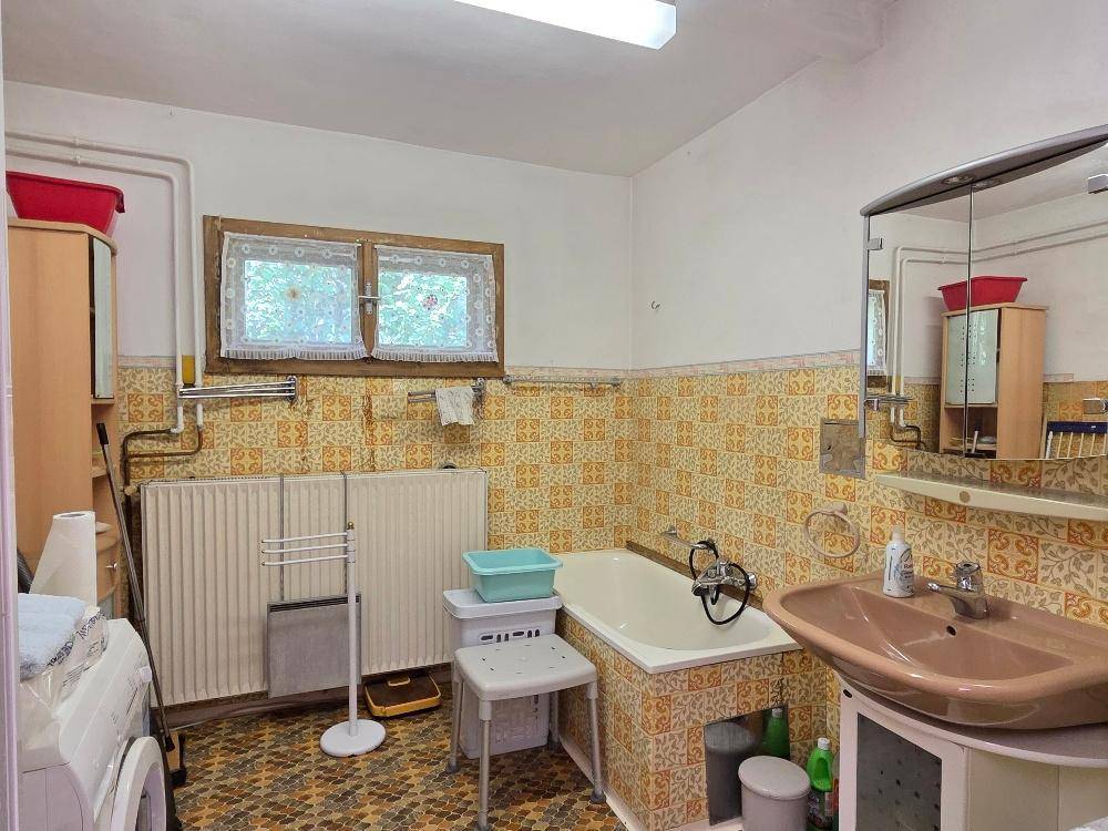 Badezimmer mit Badewanne, Waschbecken und Waschmaschine, ausgestattet mit gemusterten Fliesen.