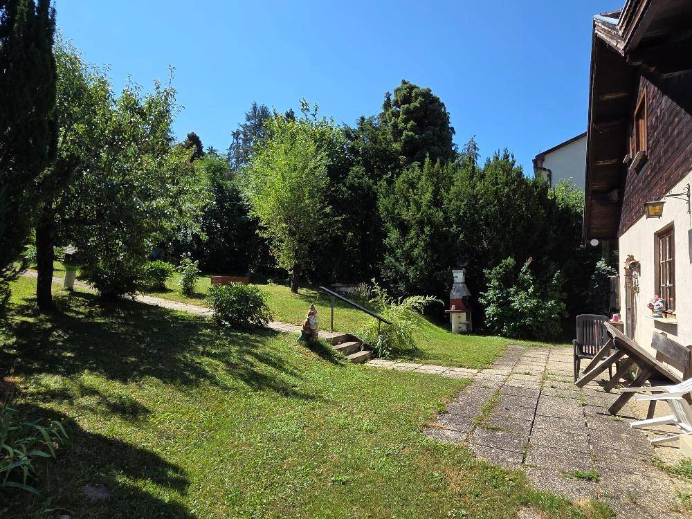 Sonniger Gartenbereich mit gepflastertem Weg, Steintreppe und gemauertem Grillplatz.