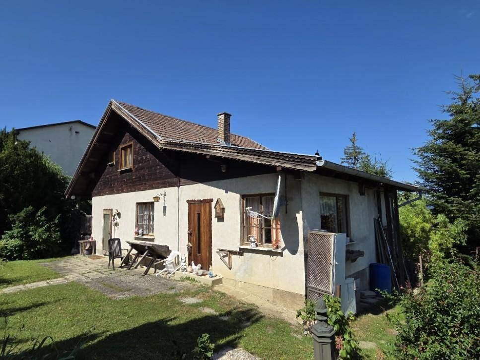 Traditionelles Haus mit Satteldach und Putzfassade, umgeben von einem grünen Garten.