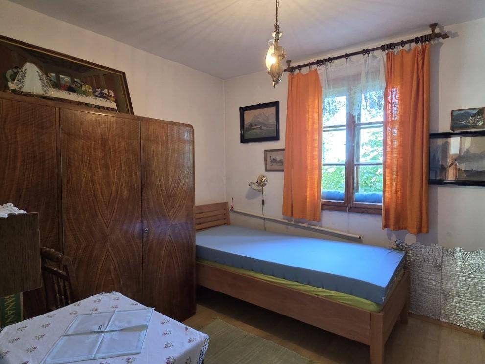 Gemütliches Schlafzimmer mit Einzelbett, großem Holzschrank und Fenster mit Vorhängen.