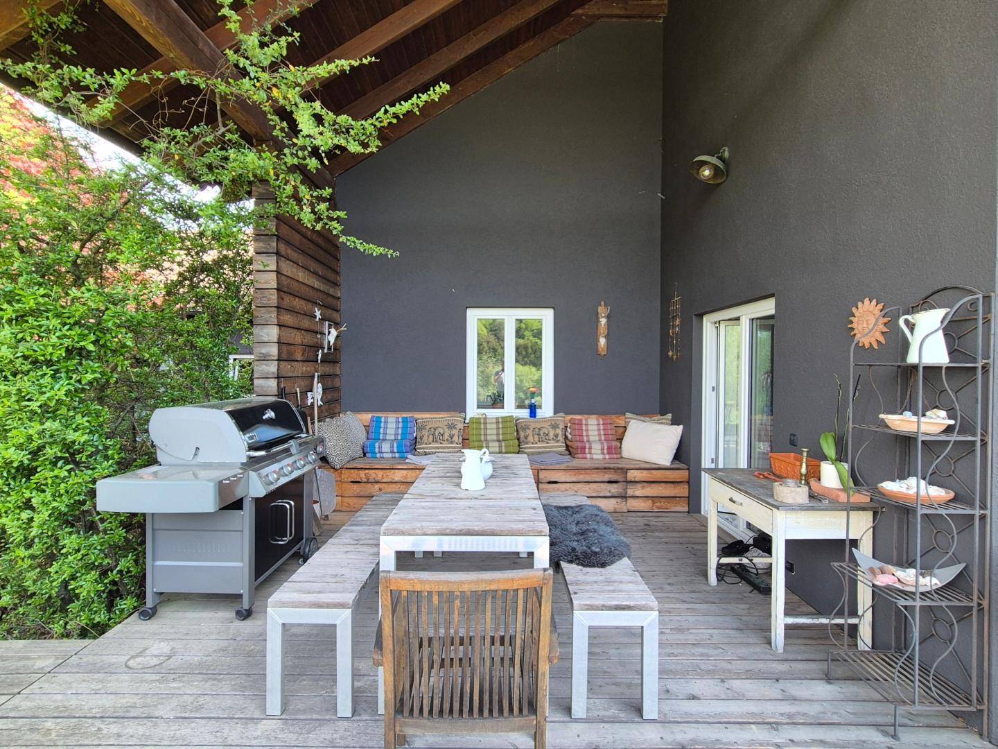 Überdachte Terrasse mit großem Esstisch, Sitzbänken, Grill und gemütlicher Lounge-Ecke für gesellige Stunden.