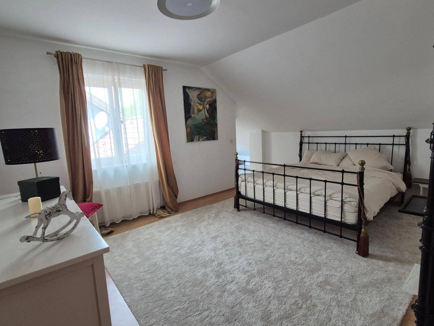 Gemütliches Schlafzimmer im Dachgeschoss mit Metallbett, Teppichboden und Fenster unter der Dachschräge.