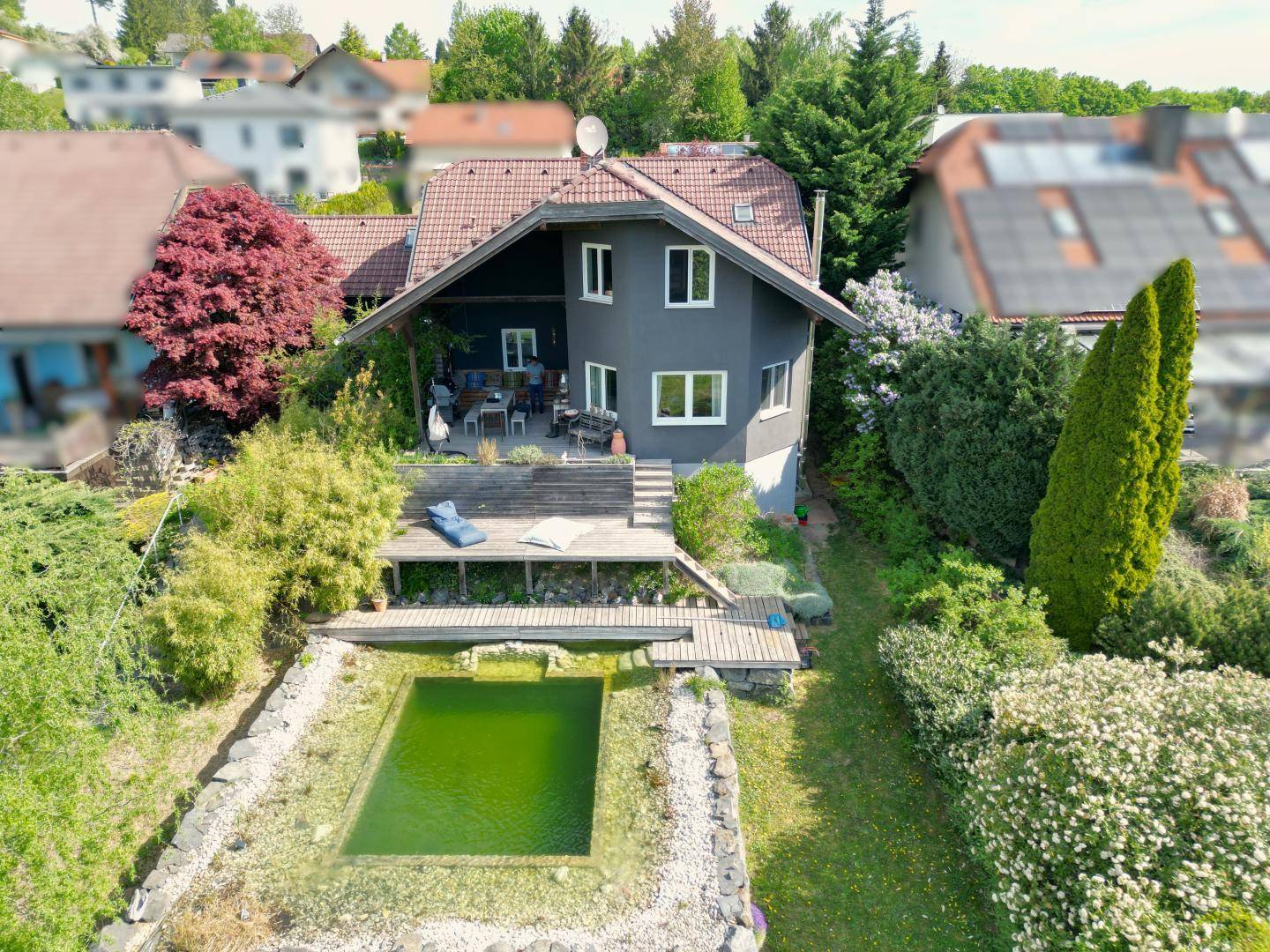 Luftaufnahme eines Hauses mit Naturpool, Holzdeck und gepflegtem Garten in einer Wohngegend.