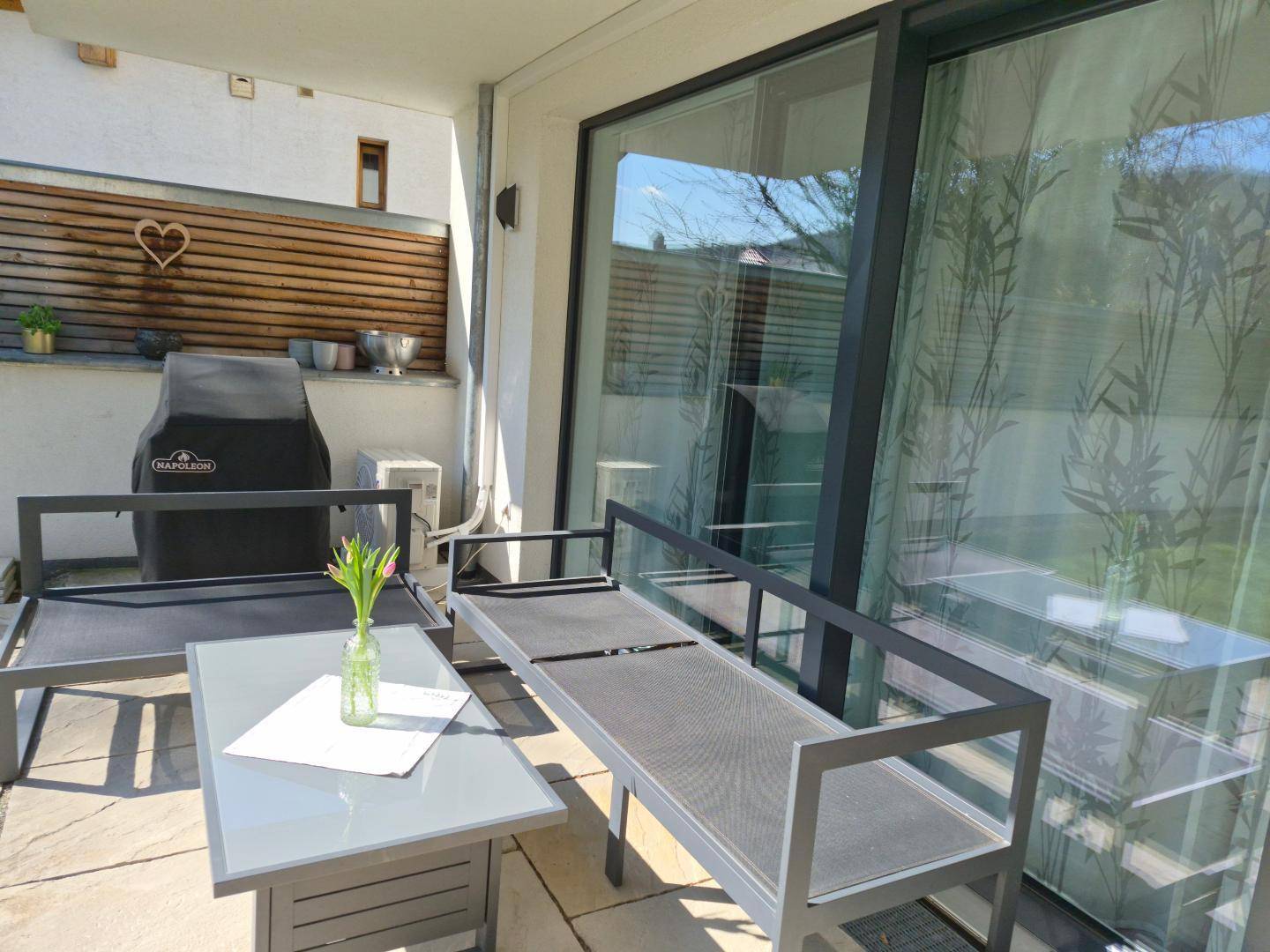 Sonniger Terrassenbereich mit modernen Lounge-Möbeln und großzügigen Glasschiebetüren zum Innenbereich.