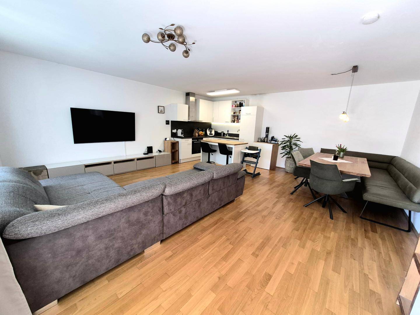 Geräumiger offener Wohn-Essbereich mit Holzboden, großem Sofa und integrierter Küche.