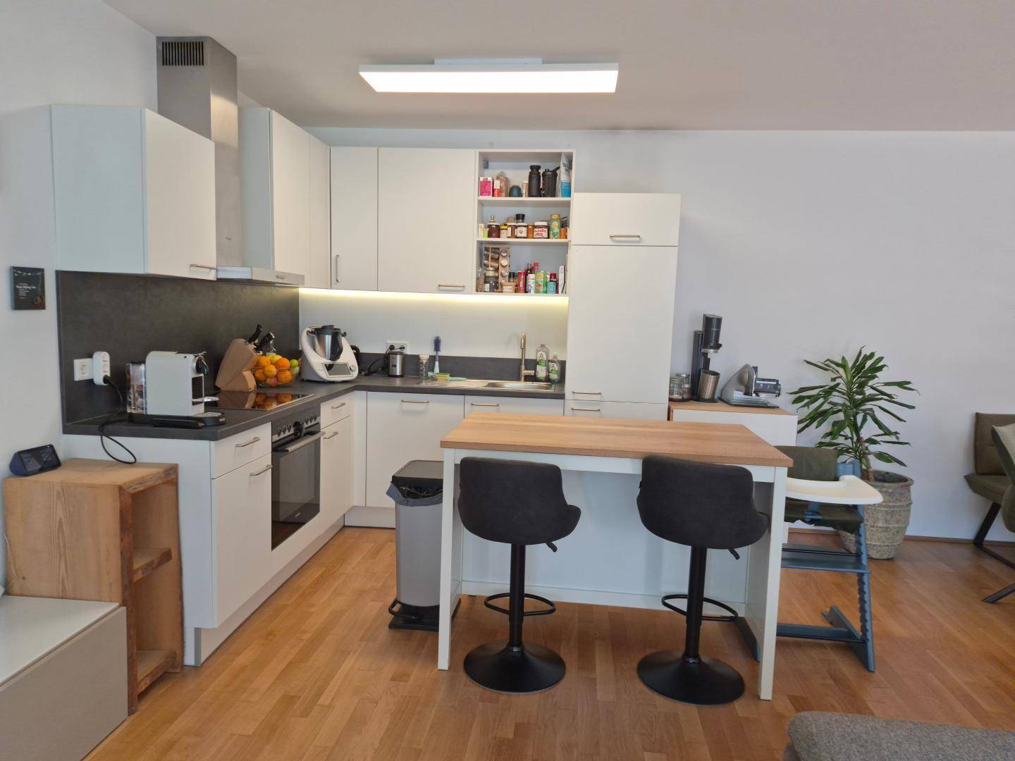 Moderne Einbauküche mit weißen Schränken, Holztheke und integrierten Geräten in offenem Wohnbereich.