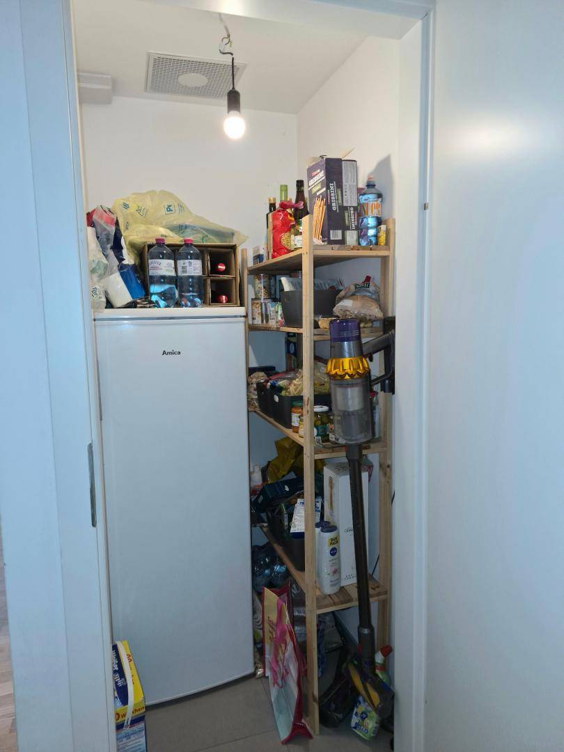 Praktischer Abstellraum mit Regalen, kleinem Kühlschrank und viel Platz für Vorräte und Haushaltsgeräte.