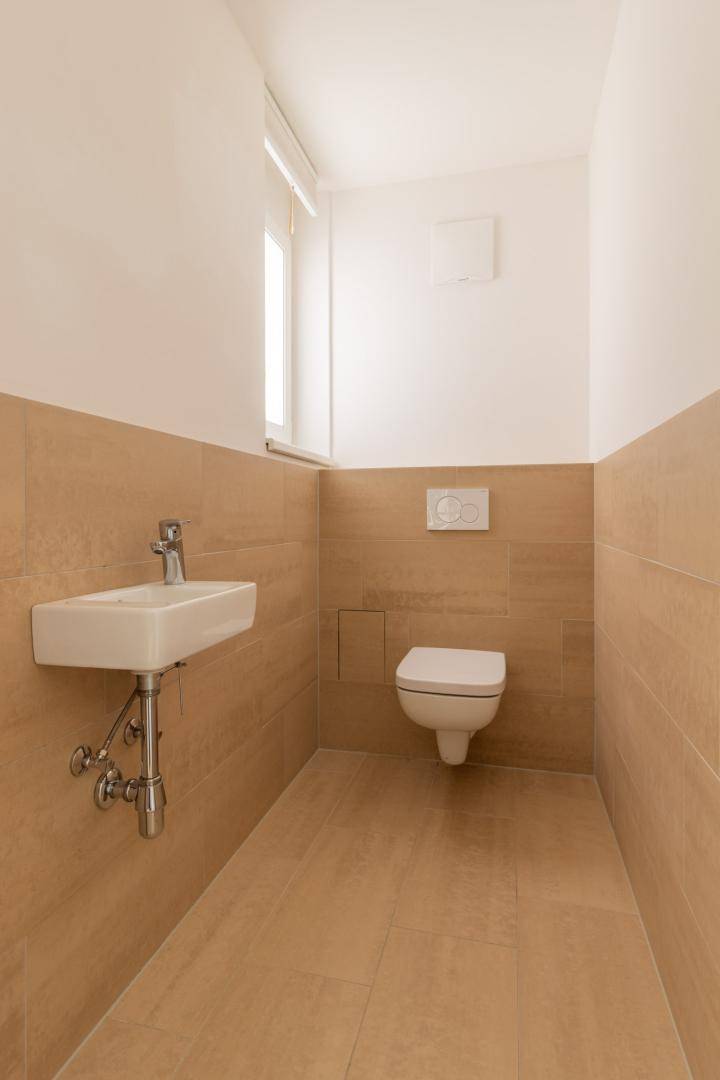 Modernes Gäste-WC mit wandhängender Toilette, kleinem Waschbecken und Fenster.