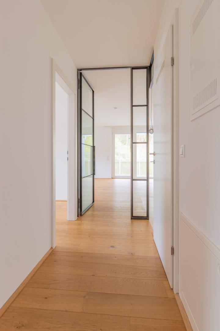 Heller Flur mit Holzboden und einer modernen Glastür, die zu den Wohnbereichen führt.