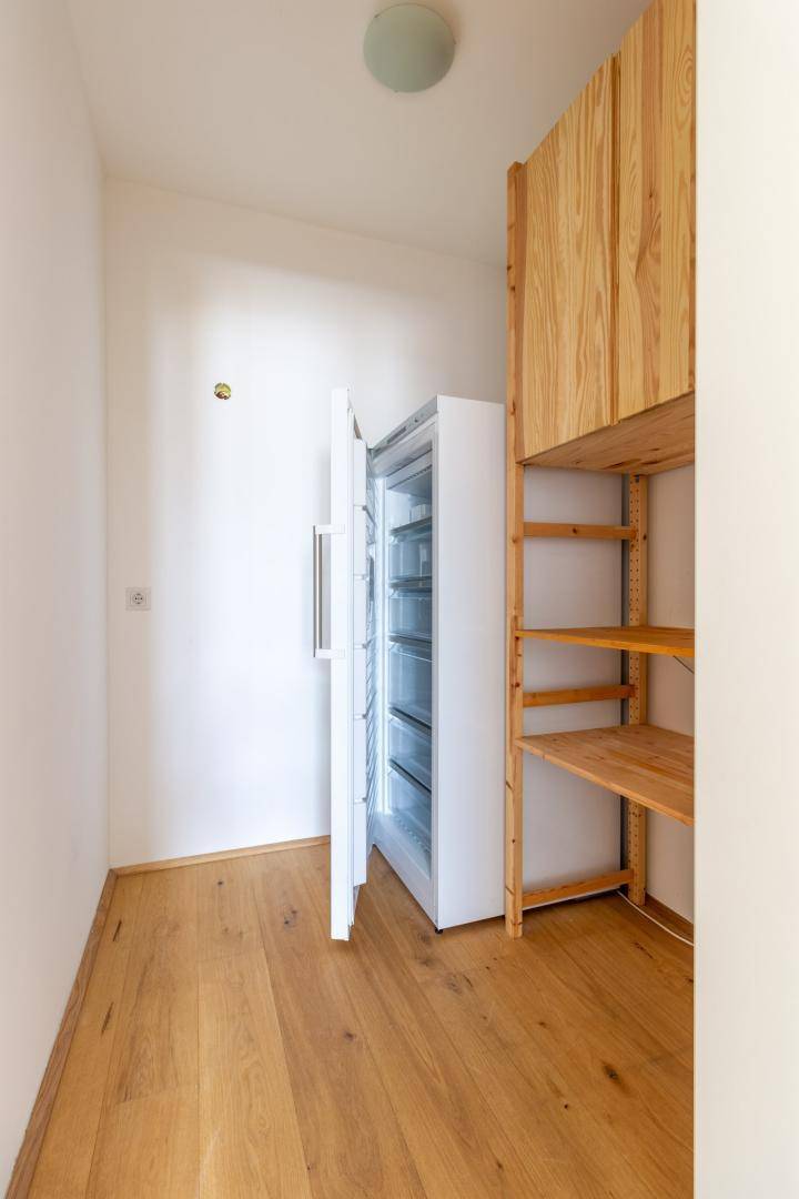Praktischer Abstellraum mit Gefrierschrank und offenen Holzregalen für zusätzlichen Stauraum.