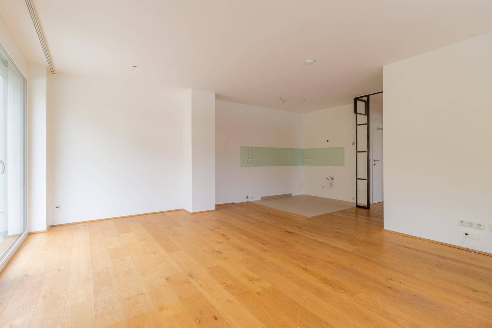 Leerer Küchenbereich mit vorbereiteten Anschlüssen und Fliesenboden, bereit für die Installation.