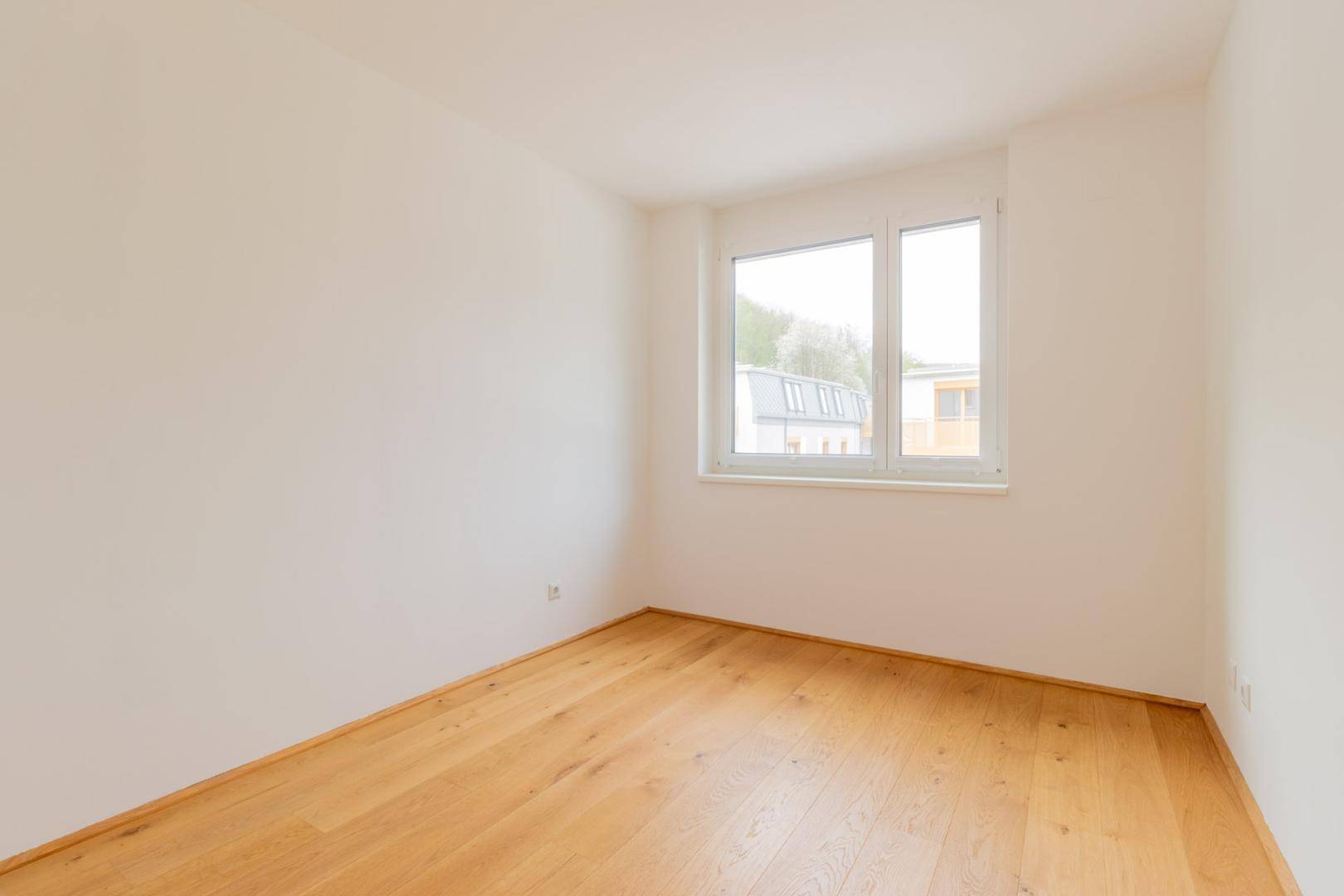 Geräumiges, leeres Schlafzimmer mit Holzboden und großem Fenster für viel Tageslicht.