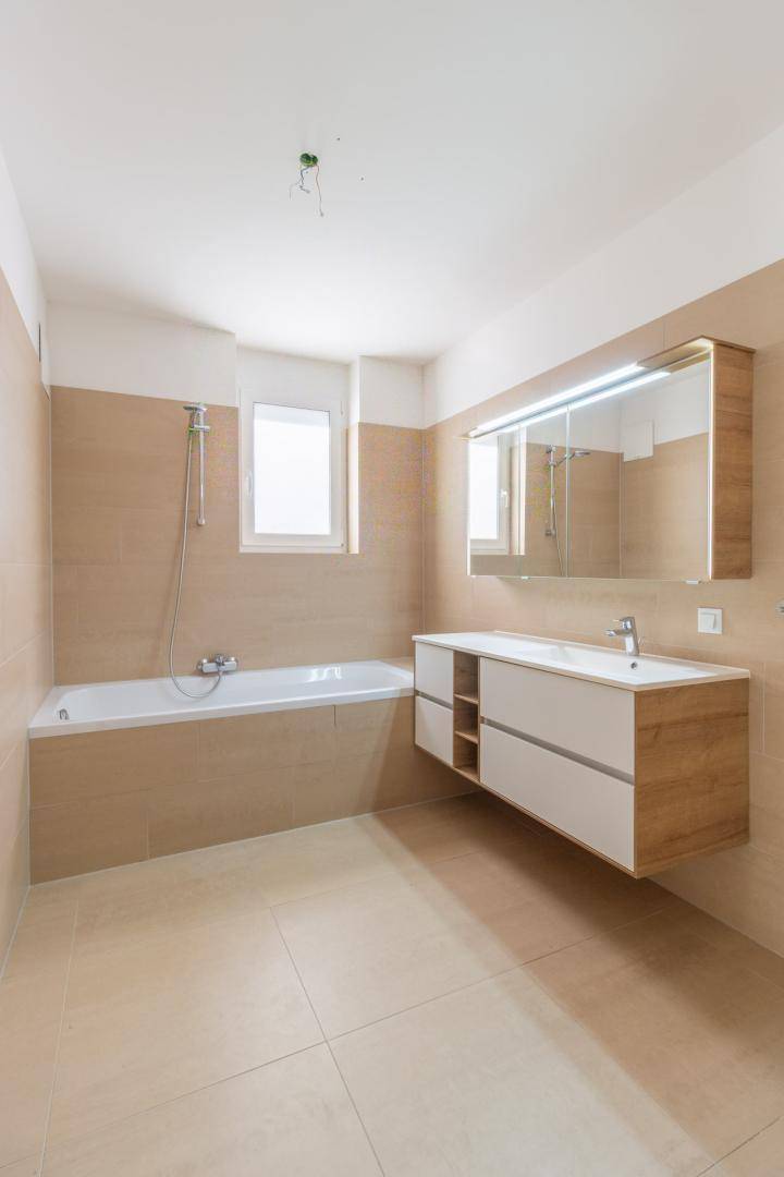 Helles Badezimmer mit Badewanne, modernem Waschtisch und großem Spiegelschrank.