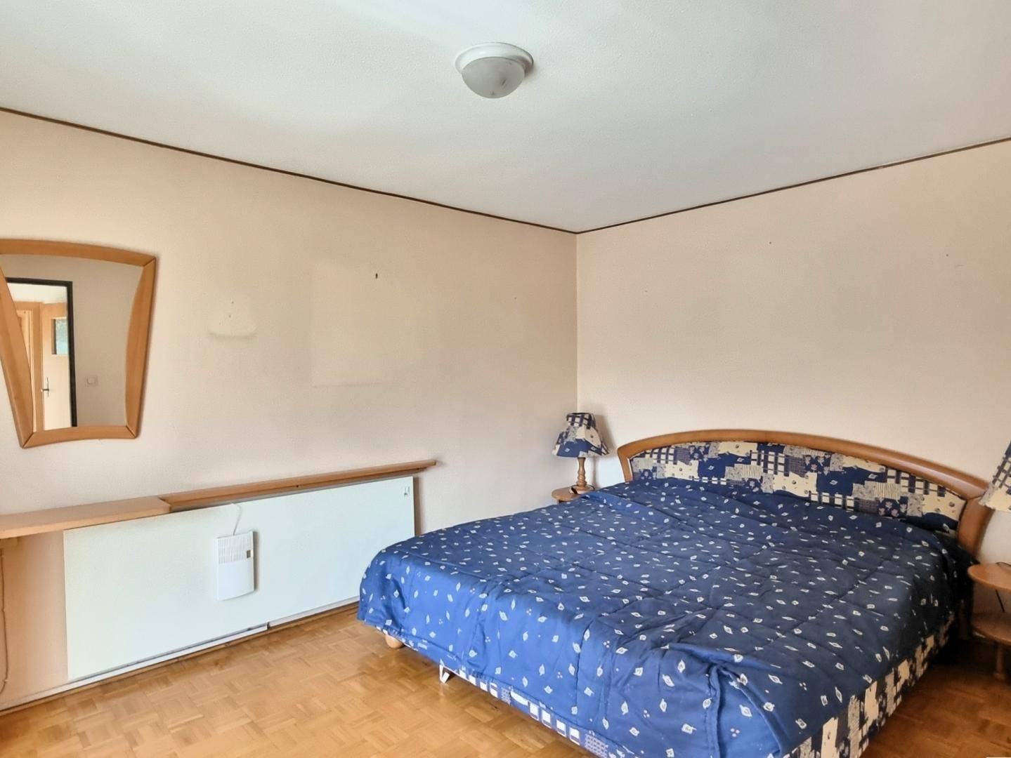 Schlafzimmer mit Parkettboden, Doppelbett und einem kleinen Nachttisch mit Lampe.