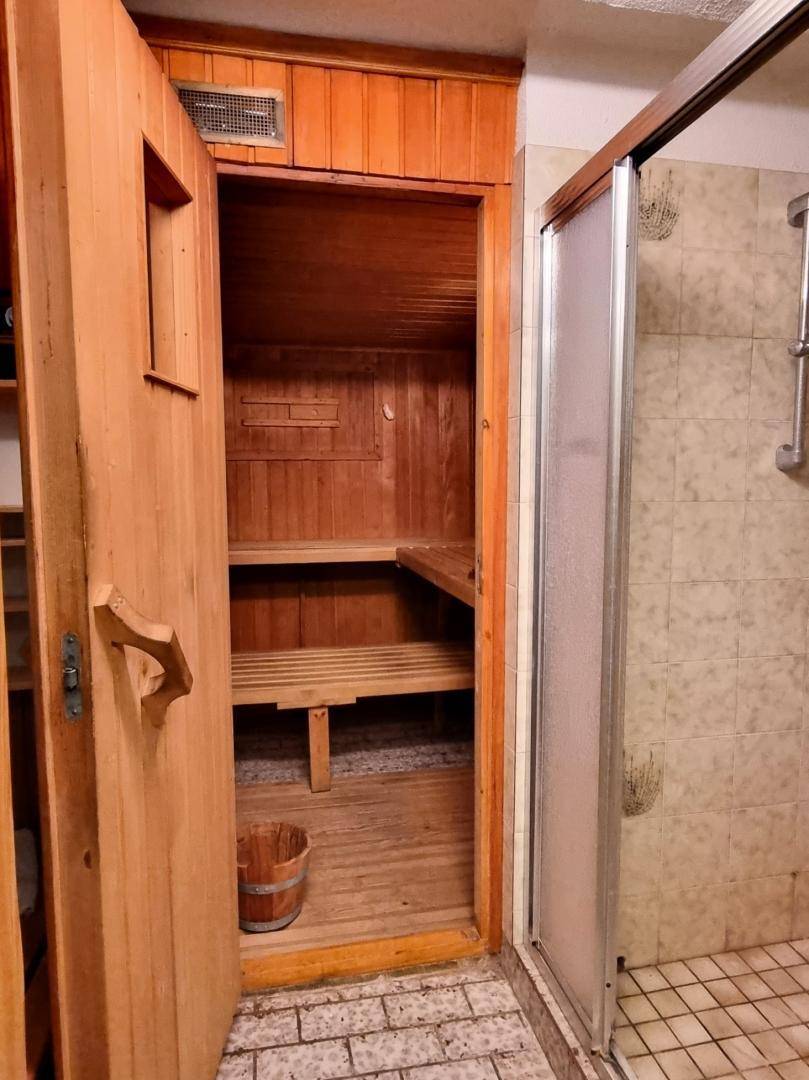 Traditionelle Holzsauna mit Bänken und Eimer, angrenzend an einen gefliesten Duschbereich.