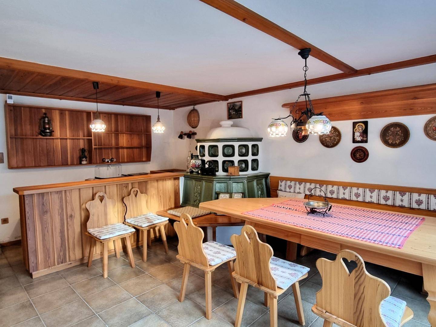 Traditioneller Essbereich mit großem Holztisch, Eckbank, Kachelofen und Holzbalkendecke.