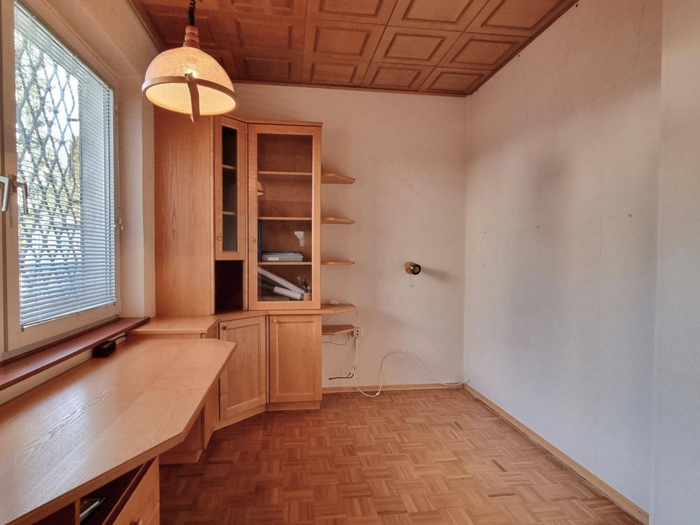 Arbeitszimmer mit Parkettboden, Holzkassettendecke und einem praktischen Einbauschreibtisch mit Regalen.