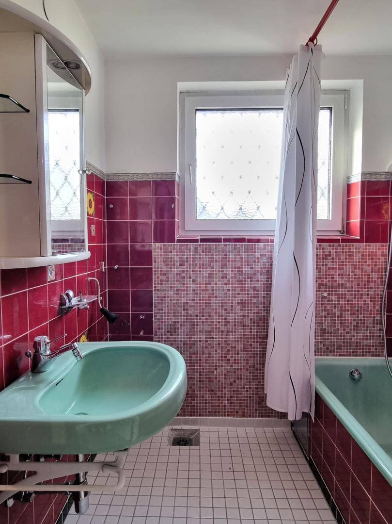 Badezimmer mit roten Fliesen, grünem Waschbecken und Badewanne, sowie einem Fenster für Tageslicht.