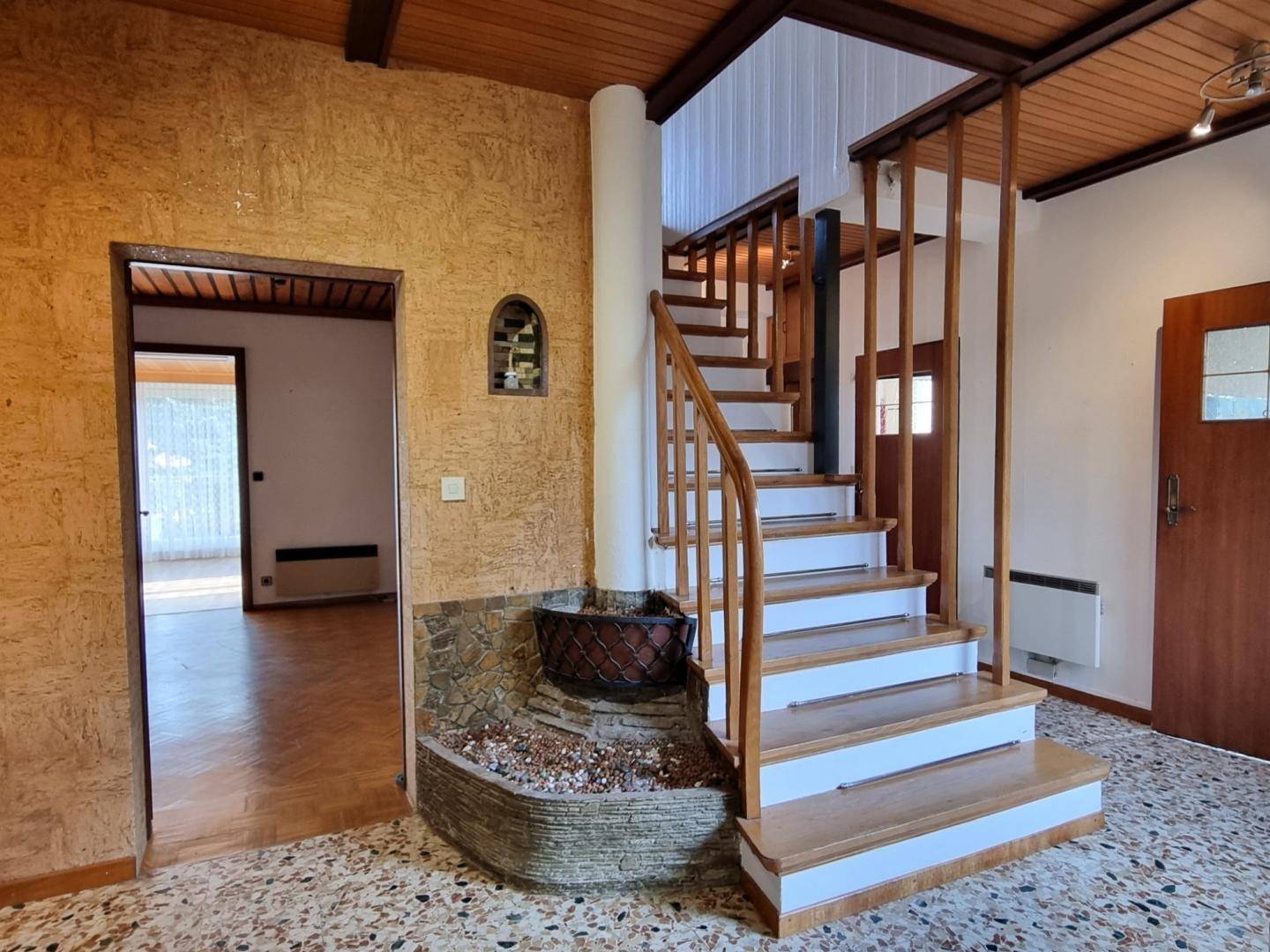 Eingangsbereich mit Holztreppe, gemustertem Fliesenboden und einer strukturierten Wandverkleidung.