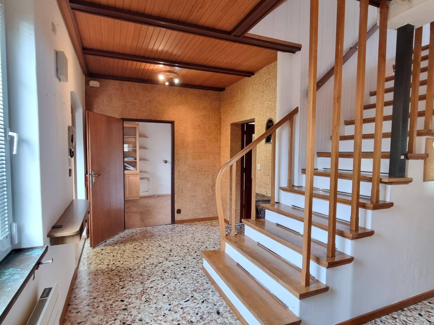 Heller Flur mit Holztreppe, Fliesenboden und Zugang zu weiteren Räumen im Haus.