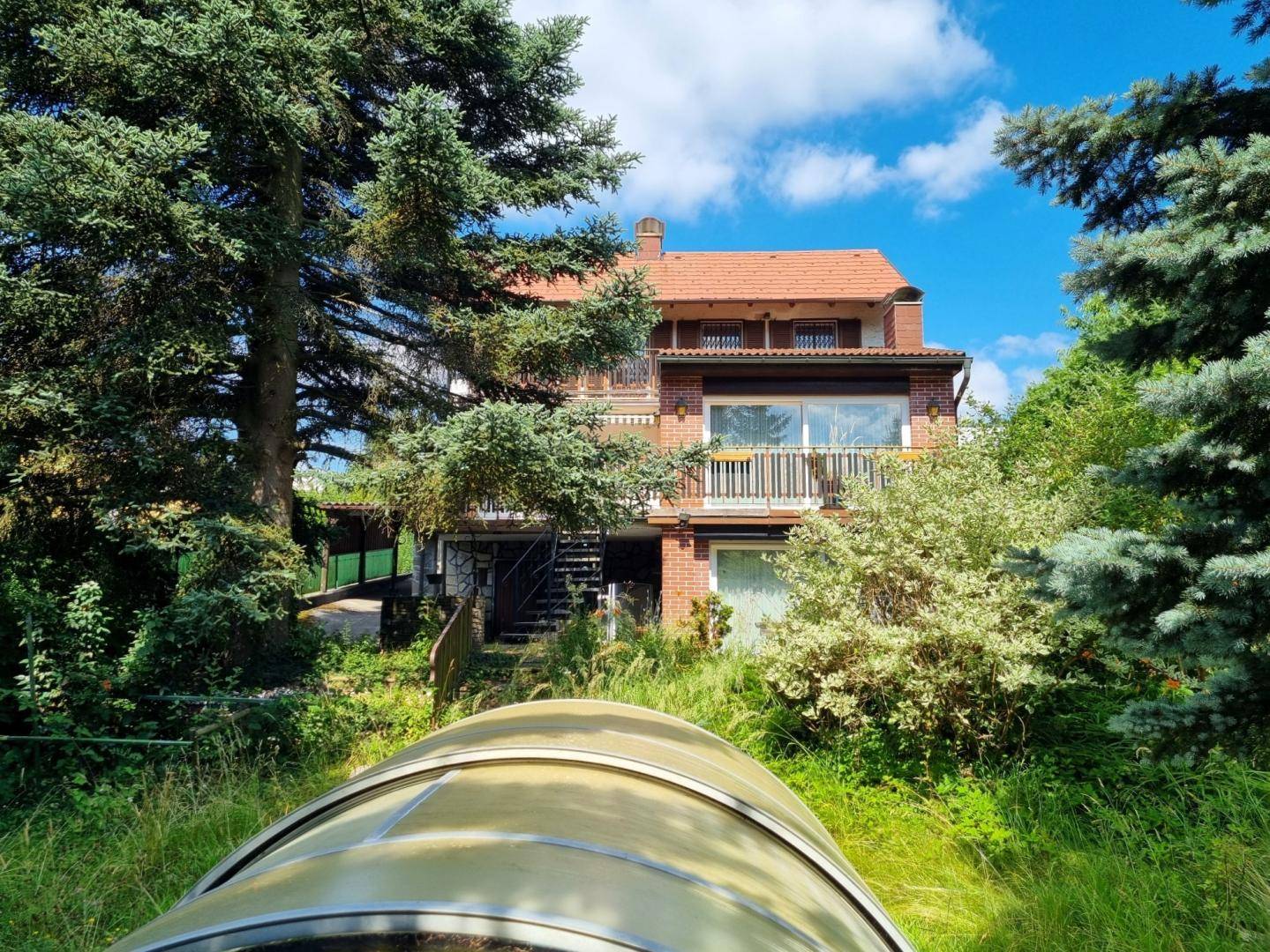 Mehrstöckiges Haus mit roten Ziegeln und Balkonen, umgeben von üppiger grüner Vegetation.