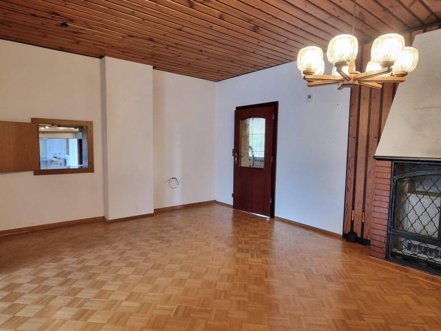 Gemütlicher Wohnbereich mit Parkettboden, Holzbalkendecke und einem traditionellen Kamin mit Ziegelverkleidung.