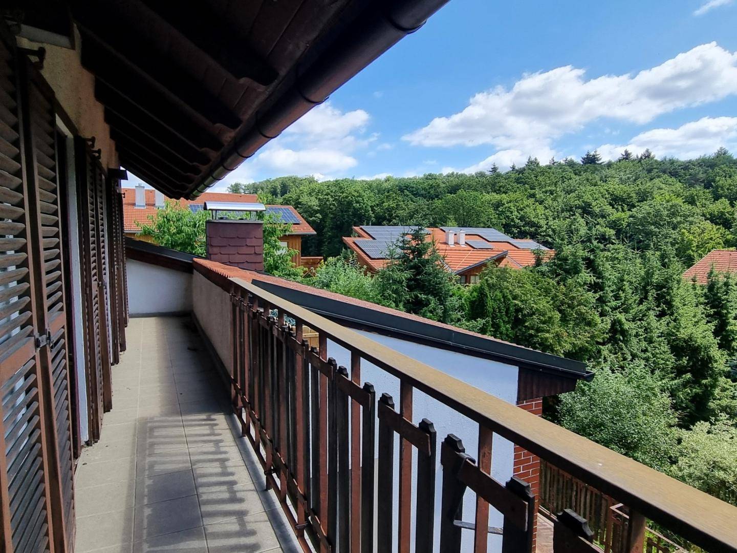 Langer Balkon mit Holzgeländer und weitem Blick über grüne Landschaft und Dächer mit Solaranlagen.