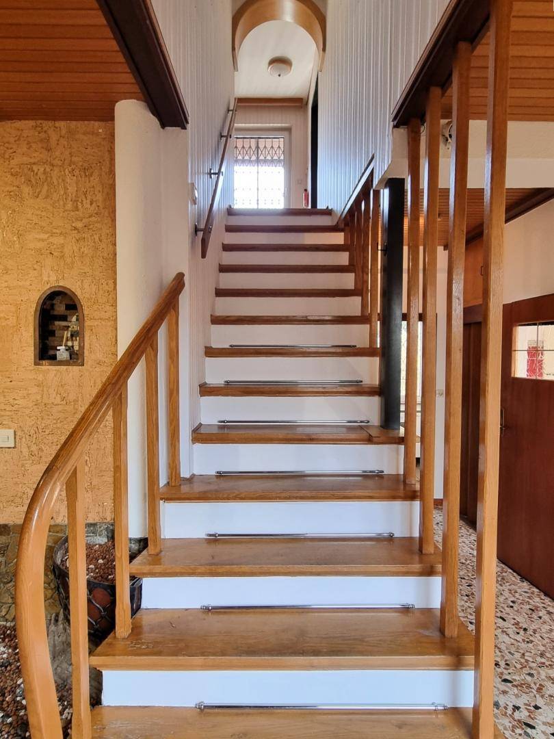 Detailansicht der Holztreppe im Flur mit weiß gestrichenen Setzstufen und Holzgeländer.