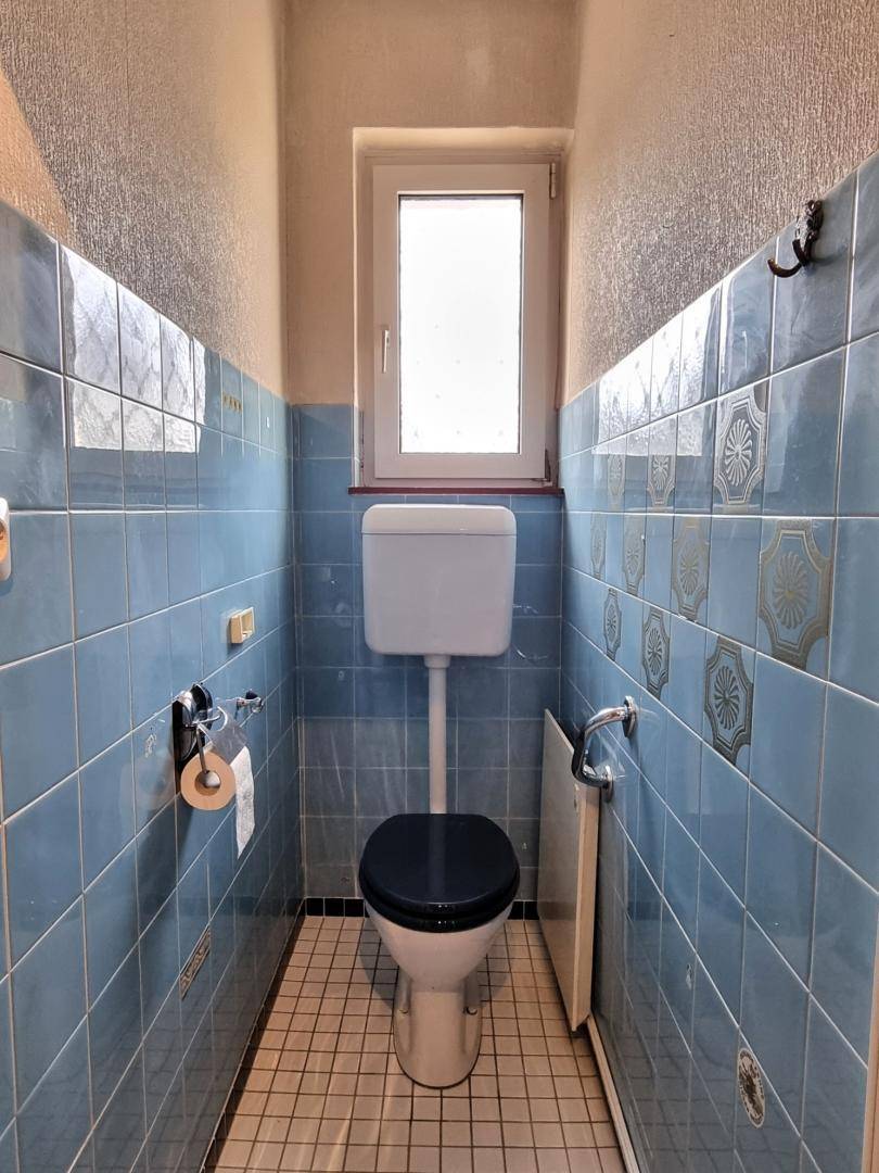 Separate Toilette mit blauen Fliesen, WC und einem kleinen Fenster für Belüftung.