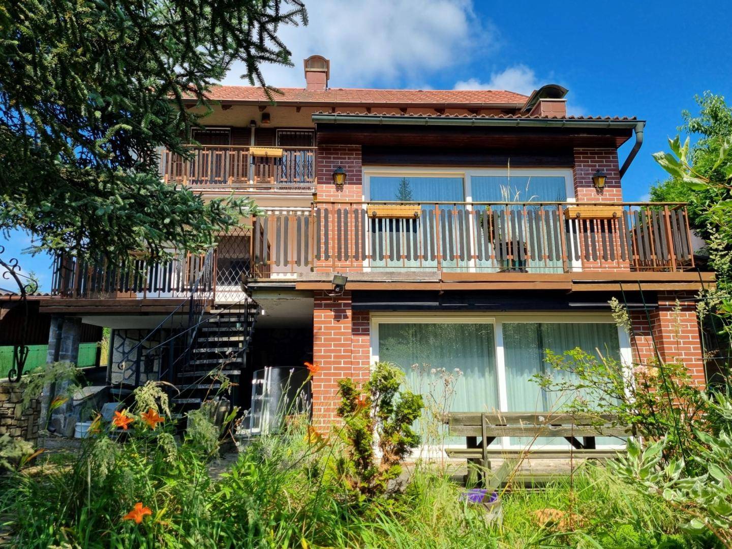 Mehrstöckiges Haus mit Ziegelfassade, mehreren Balkonen und traditionellen Holzgeländern, umgeben von Natur.