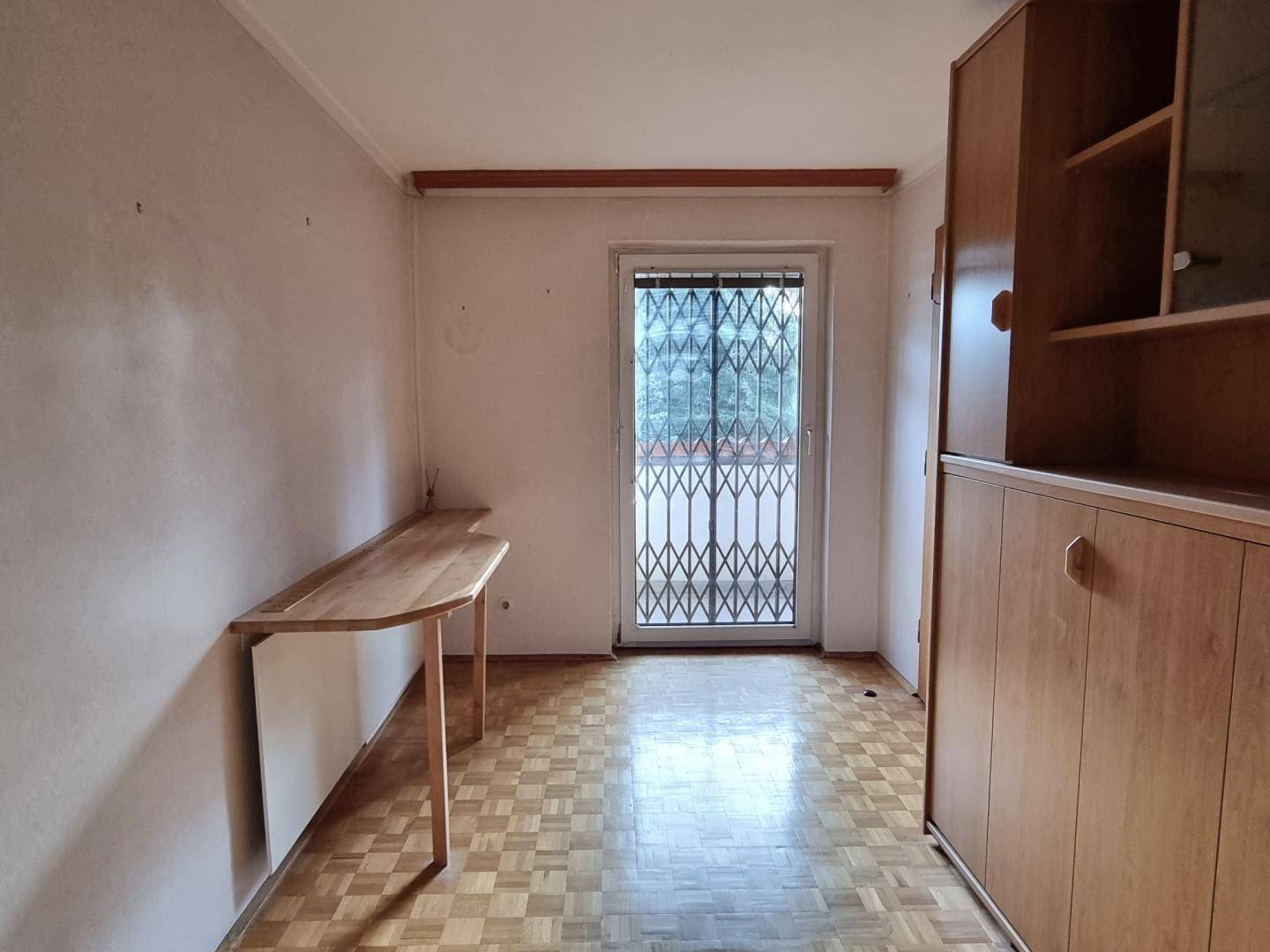 Schlafzimmer mit Parkettboden, Holzschrank und Zugang zu einem Außenbereich mit Gitter.