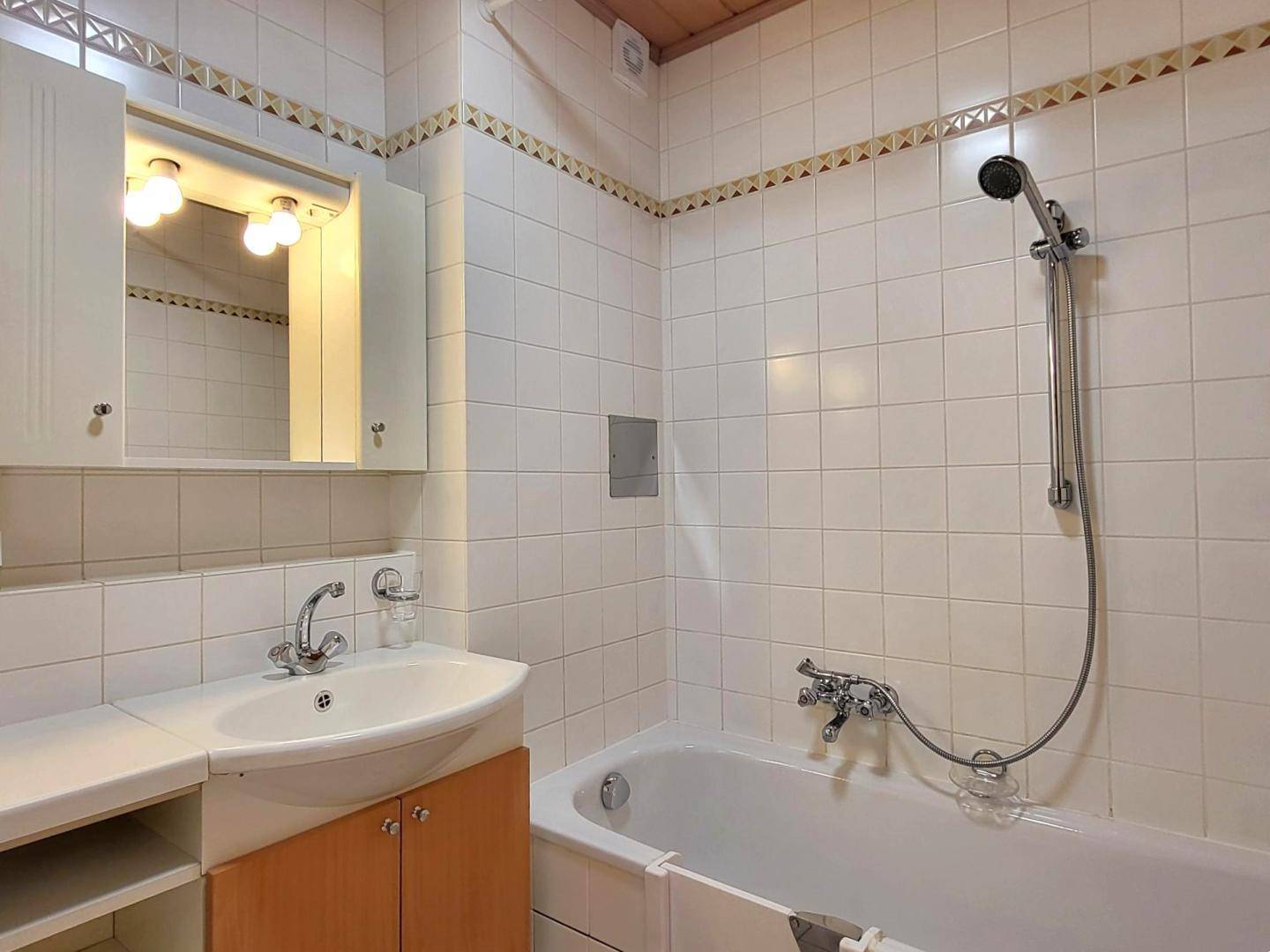 Gefliestes Badezimmer mit Badewanne, Duschkopf und Waschbecken mit Spiegelschrank.