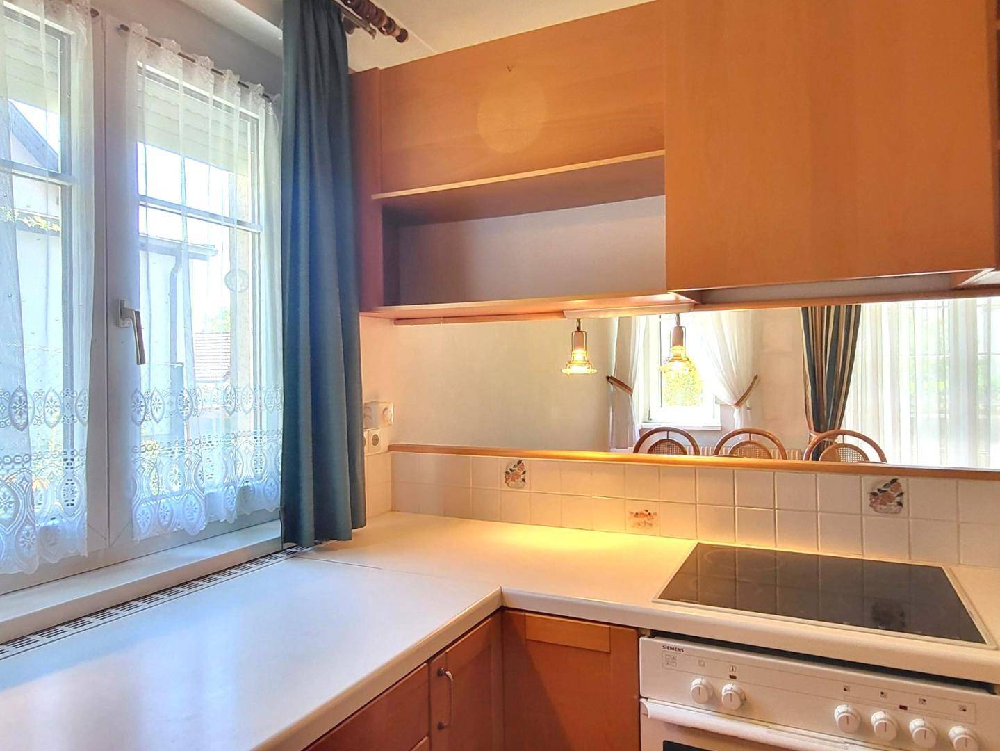 Küche mit Fenster, weißer Arbeitsplatte und integriertem Kochfeld.